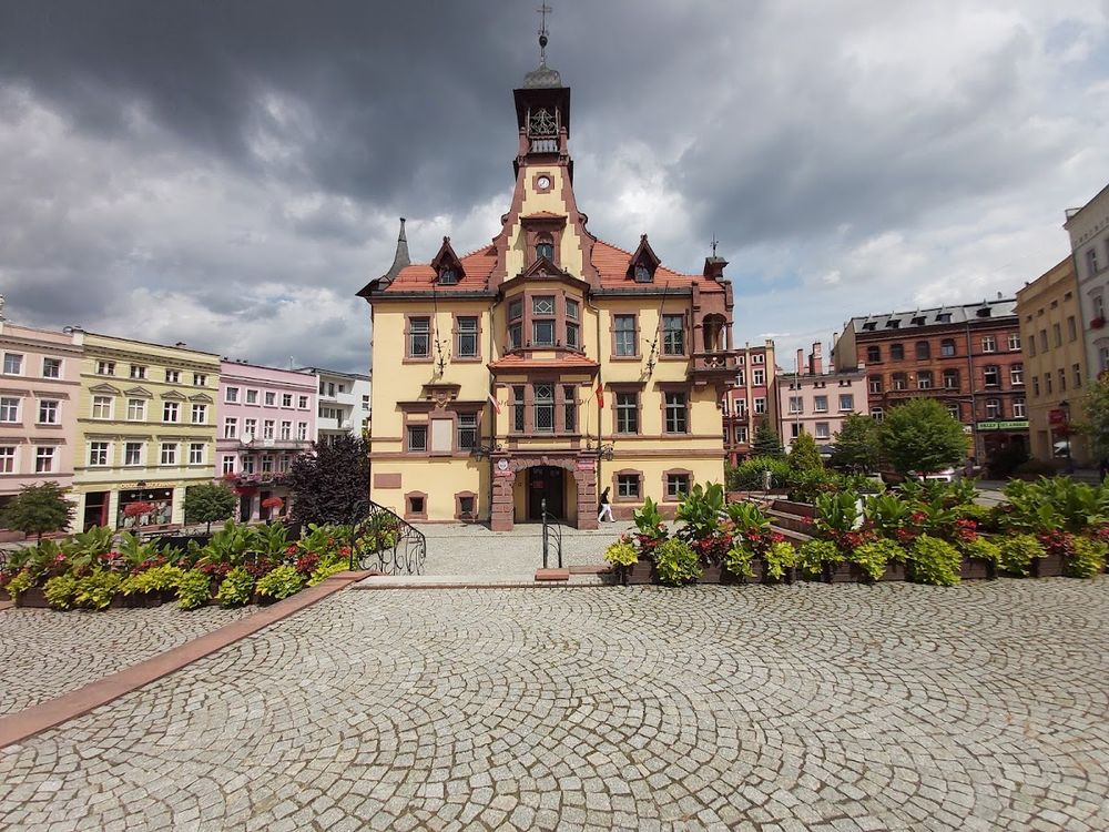 Plac miejski z zabytkowymi budynkami o liliowym słońcu pod niebem.