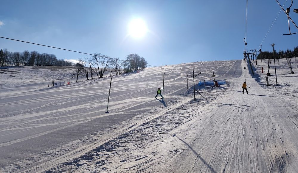 Narciarze na trasie w Olešnice pod głębokim błękitem nieba.