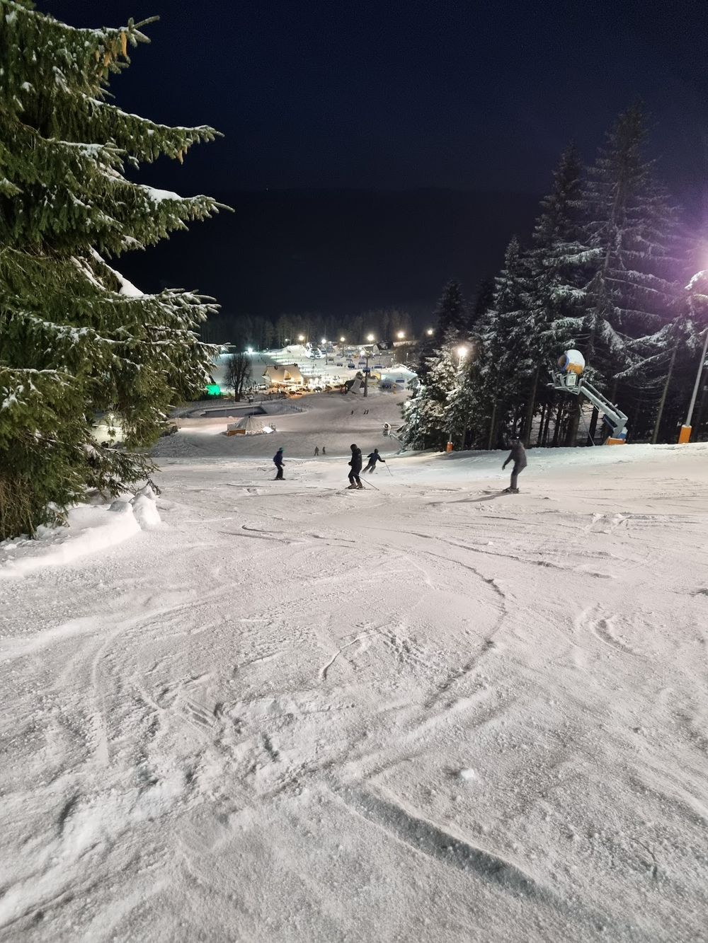 Narciarze podczas nocnych zjazdów na oświetlonym stoku Nartoramy.