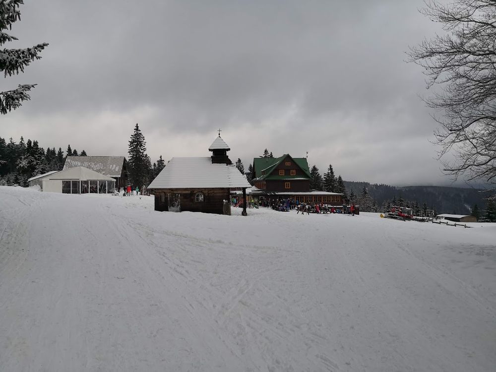 Mały, nastrojowy domek w Bielicach zasypany śniegiem pod błękitnym niebem.