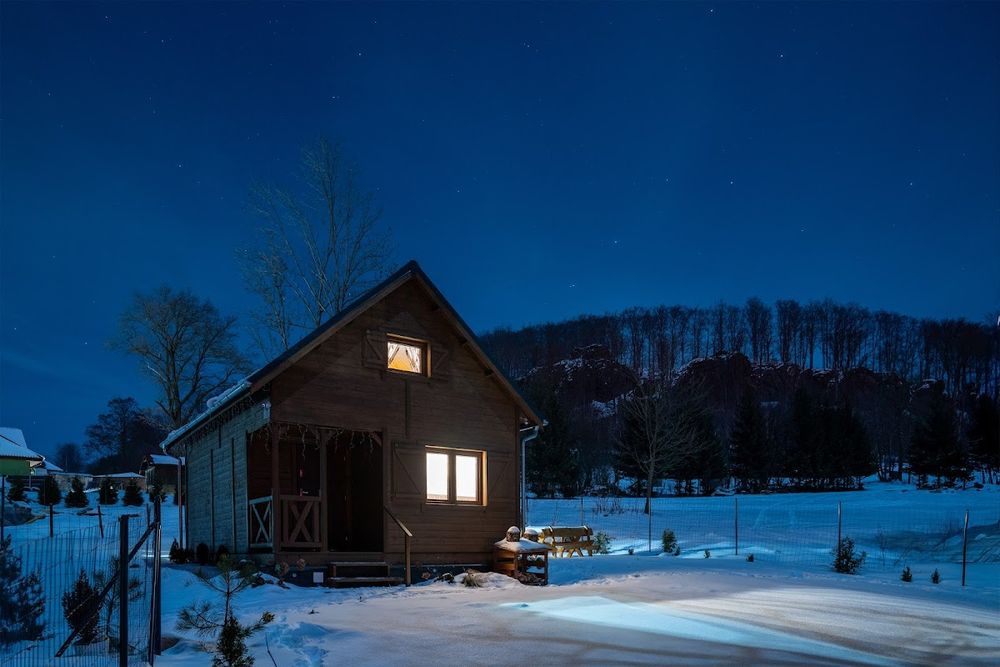 Nocny widok na oświetlony domek na tle górskiej panoramy.