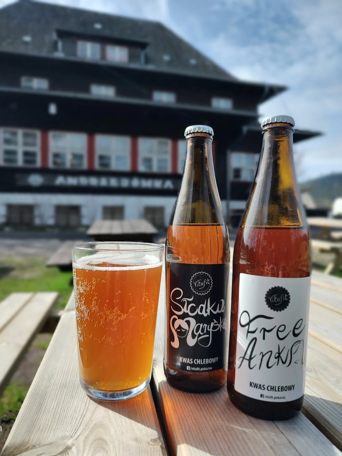 Butelki piwa rzemieślniczego oraz szklanka z piwem na drewnianym stole.