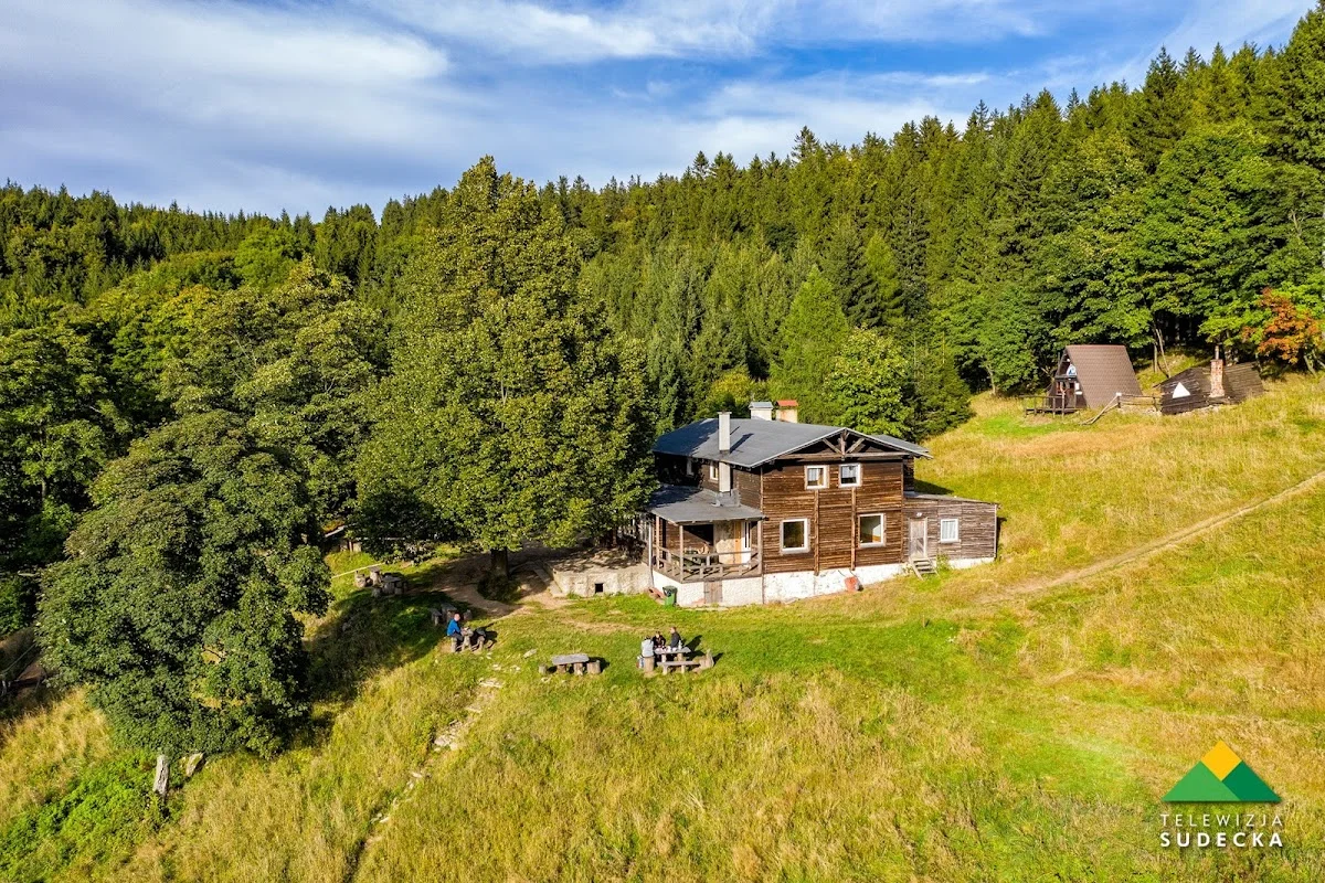 Budynek o szarej elewacji wśród górskich lasów.