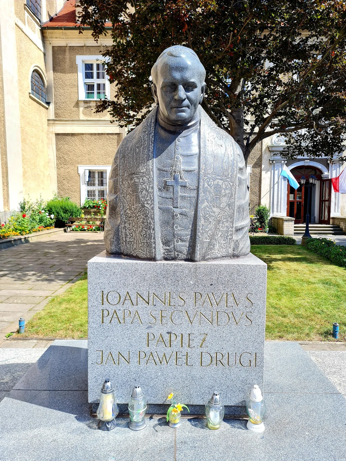 Pomnik papieża Jana Pawła II przed kościołem pod słońcem pod niebem.