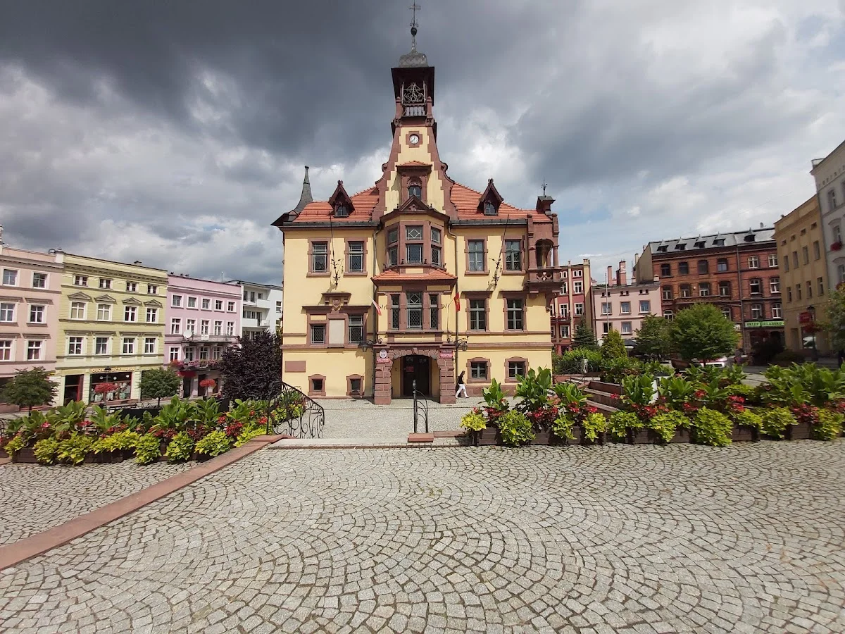 Plac miejski z zabytkowymi budynkami o liliowym słońcu pod niebem.