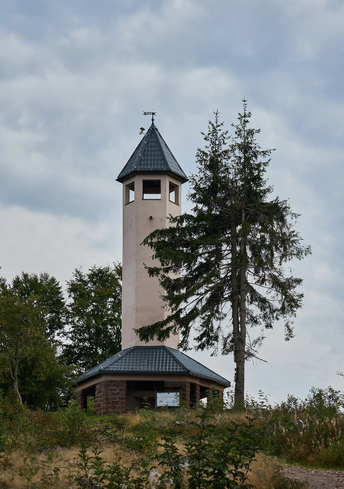 Biała wieża widokowa o nastrojowej formie pośród zielonych drzew.